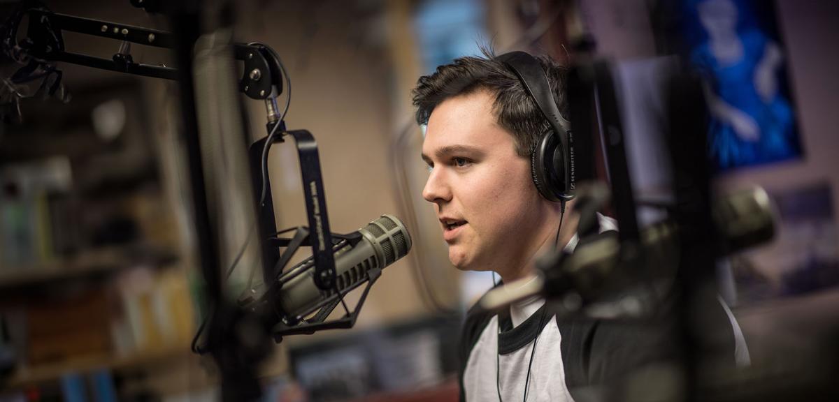 A student wearing headphones speaks into a microphone in a radio studio at Westfield State University.