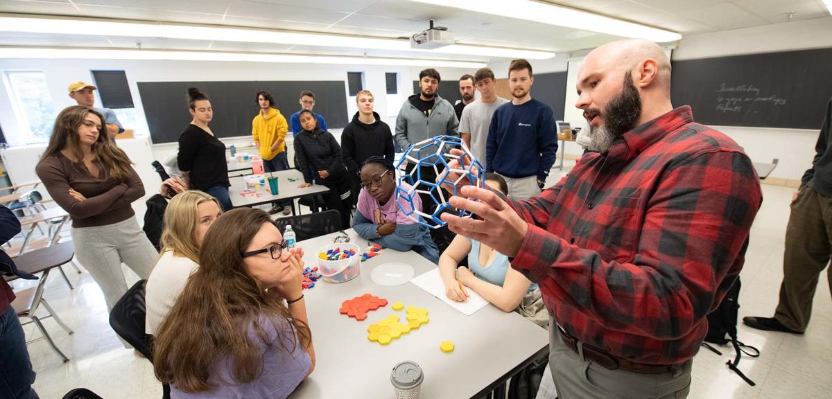 A math professor uses a 3D model to demonstrate mathematical concepts to students in a classroom.