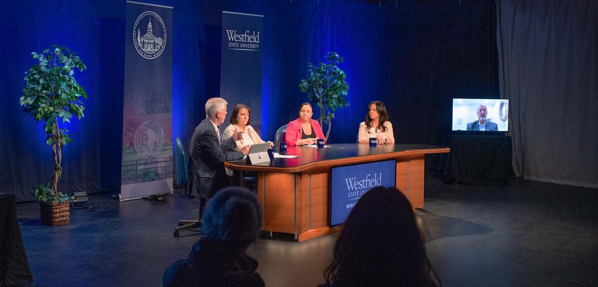 State and local government leaders sit at a large desk on a stage during a discussion about career opportunities in municipal government.