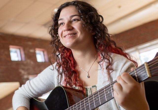 Music student holding a guitar smiling.