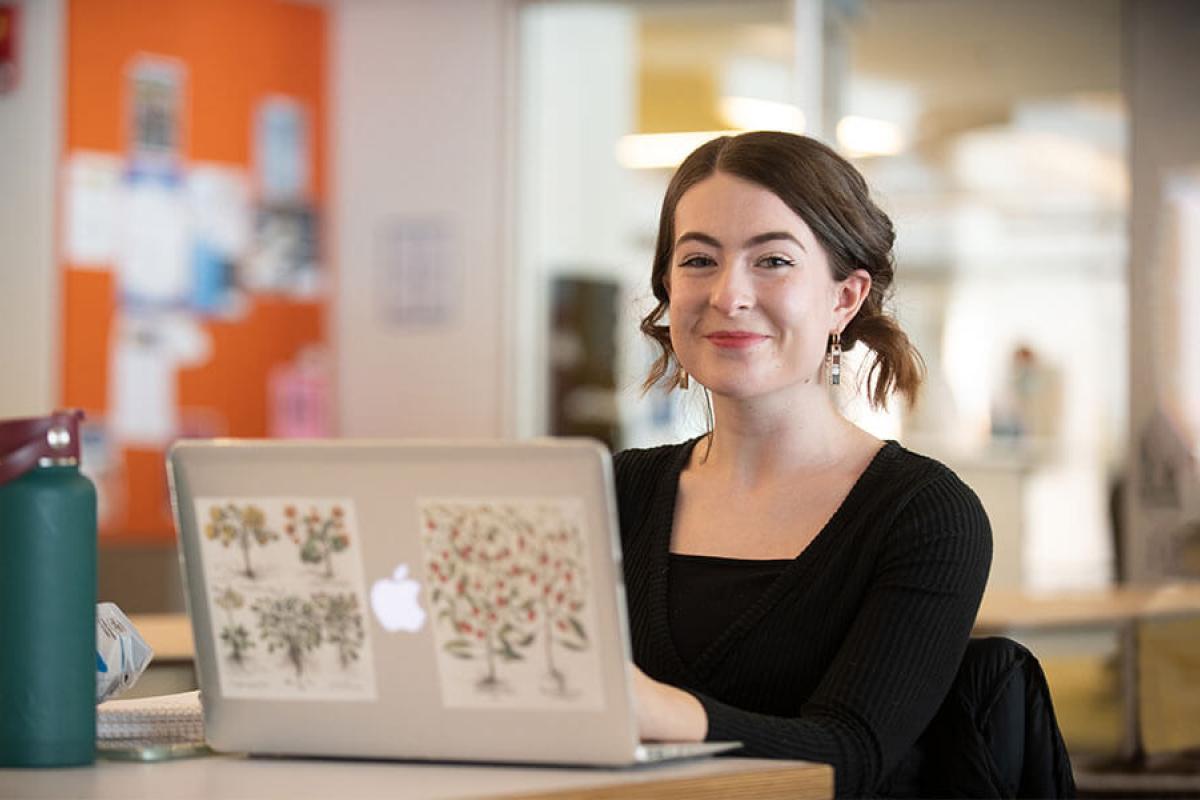 A student smiles while working on their laptop.