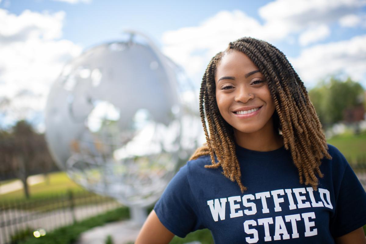 Student standing at the campus globe smiling wearing a WSU shirt.