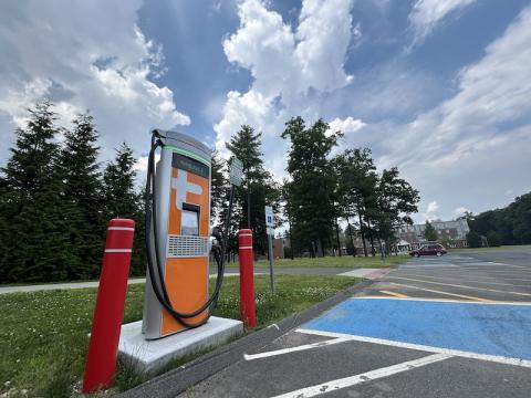 The electric vehicle charger in the Commuter Lot. It is an orange machine and flanked by two, red safety pillars.