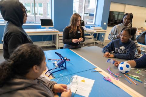 Grace Templeton of the RIDE Center during the Junior Discover program, an initiative that allows schools in the Springfield and Holyoke school systems to experience campus life. They are working on a project at the RIDE Center, and several students sit around her at their desk.