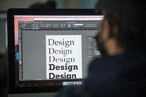 A stock photo of a student sitting in front of a computer, with him experimenting with typography in a graphic design class.