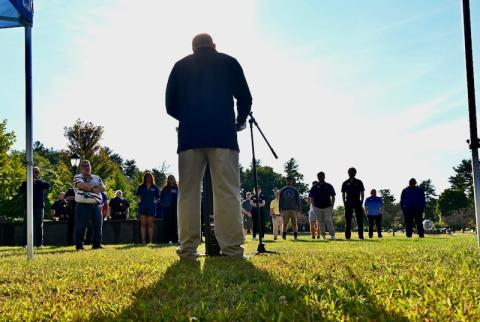 A photo from September 11's Moment of Silence Ceremony. Robert Vigneault, Assistant Director of the Office of Veteran and Military Services, is giving remarks at a small podium and microphone to a crowd of people who came to pay their respects.