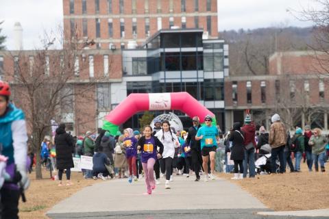 Girls on the Run, hosted on November 24. A crowd of people run towards the camera in front of the Ely Campus Center for the 5K event.