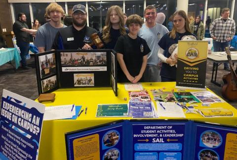 Group of students stand behind the Campus Activities Board table with display posters and handouts 