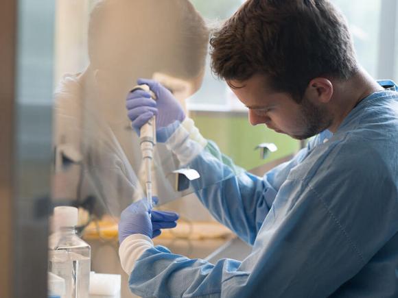  A student wearing protective clothing and gloves conducts an experiment in a laboratory setting.