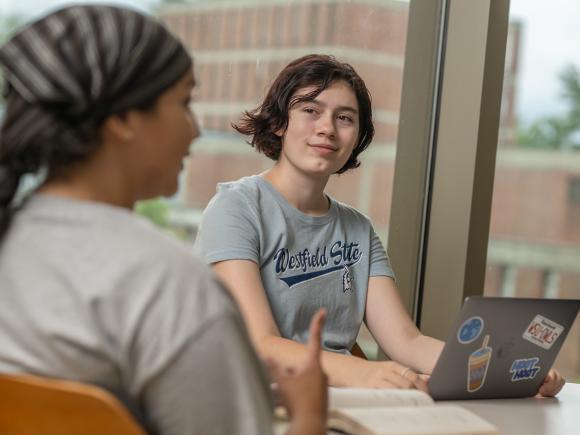 English student smiling with a laptop wearing a WSU shirt.