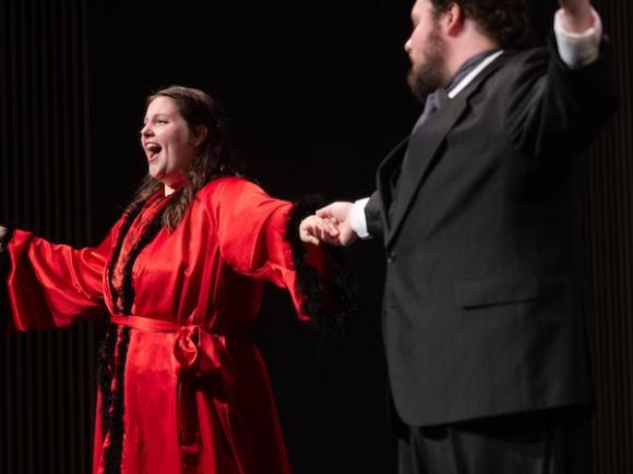 A women in a red robe singing on stage next to her co-star in a suit, as part of The Bat’s Revenge, a lively operetta based on Johann Strauss II's Die Fledermaus, with a fresh, modern twist set in 1930s Hollywood. 