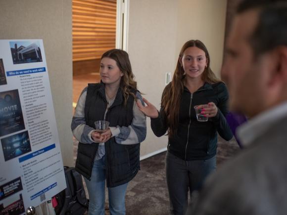 Two young women presenting a poster board and their idea to a "Shark" as part of Discover Westfield's Shark Tank event.