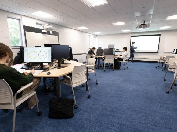 Students work at computer stations while an instructor leads a class in Westfield State University's newly renovated Center for Interdisciplinary Informatics, featuring collaborative workspaces and technology for hands-on learning.
