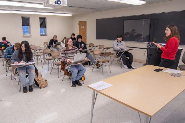 A professor stands at the front of a classroom while instructing their students.