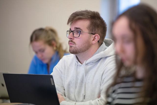 A student looks up from their laptop while seating at a desk in a classroom.