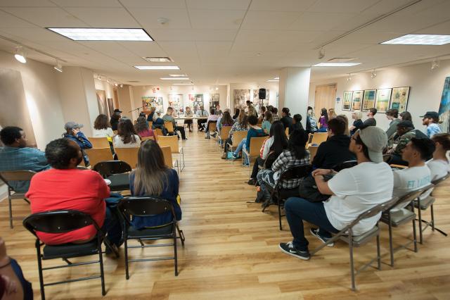 Art exhibit with students in rows of chairs.