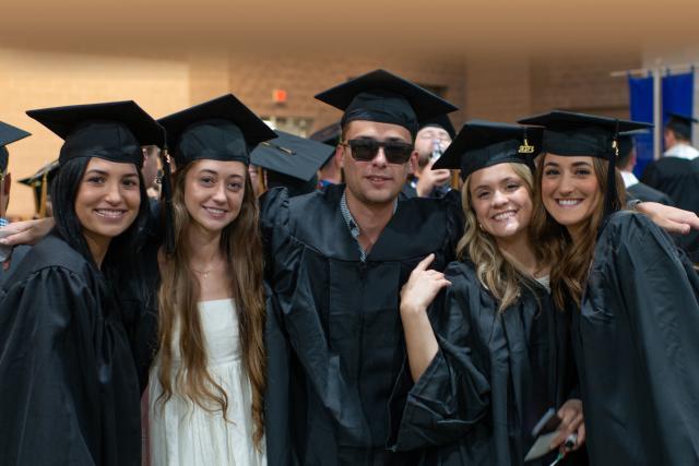 5 Westfield State University students in their caps and gowns smile for the camera