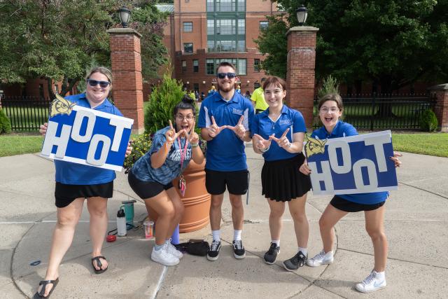 Westfield State Orientation Leaders hold up Hoot signs, and make Westfield W's with their hands as they mug for the camera.