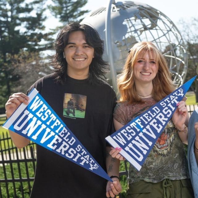 Two students smiling at campus globe holding WSU pennant flags.