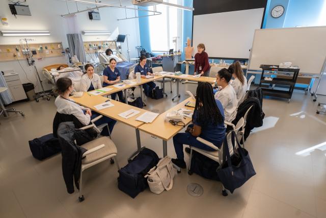 Students and faculty engaged in a discussion inside the Nursing Department's SIM Lab.