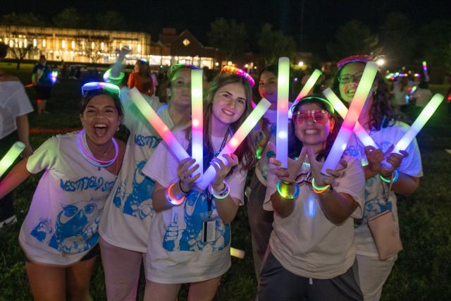 Students smiling and holding glow sticks during Welcome Week.