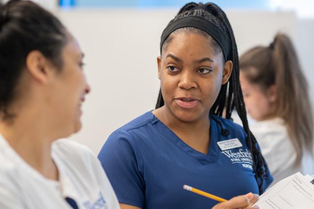 Nursing student speaking with another student holding a pencil.