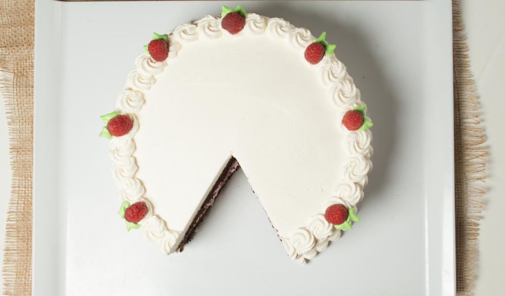 Chocolate cake with vanilla icing and raspberry accents on the top. Served on a white plate.