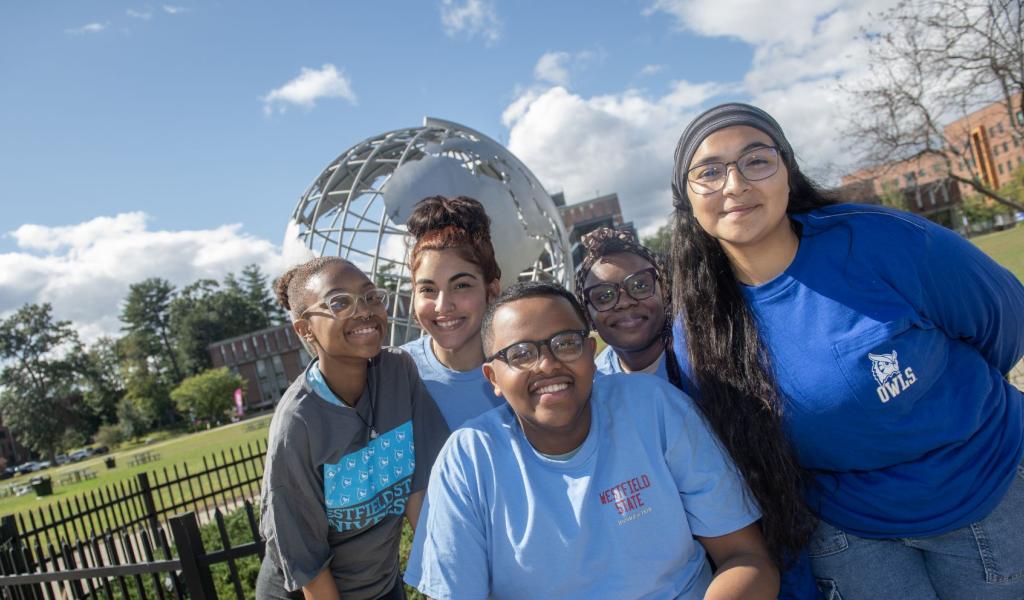 Five students smile while posing for a photo in front of the Westfield State University globe sculpture.
