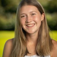 Student tour guide Shea Hamel. She is smiling and standing in an open field, with the background blurred behind her. 