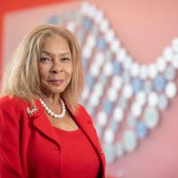 President Linda Thompson of Westfield State. She's wearing a red suit and is posed before a red mosaic wall in the Nettie Stevens Science and Innovcation building