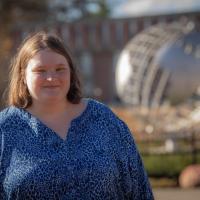 Melissa Costello, Class of 2022, posing in front of the campus globe. She's wearing a blue blouse and has the globe unfocused in the backround.