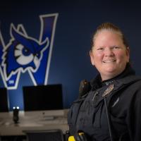 Officer McCue of Westfield State. She is wearing her police uniform and posing in front of a navy-blue Nestor mural.